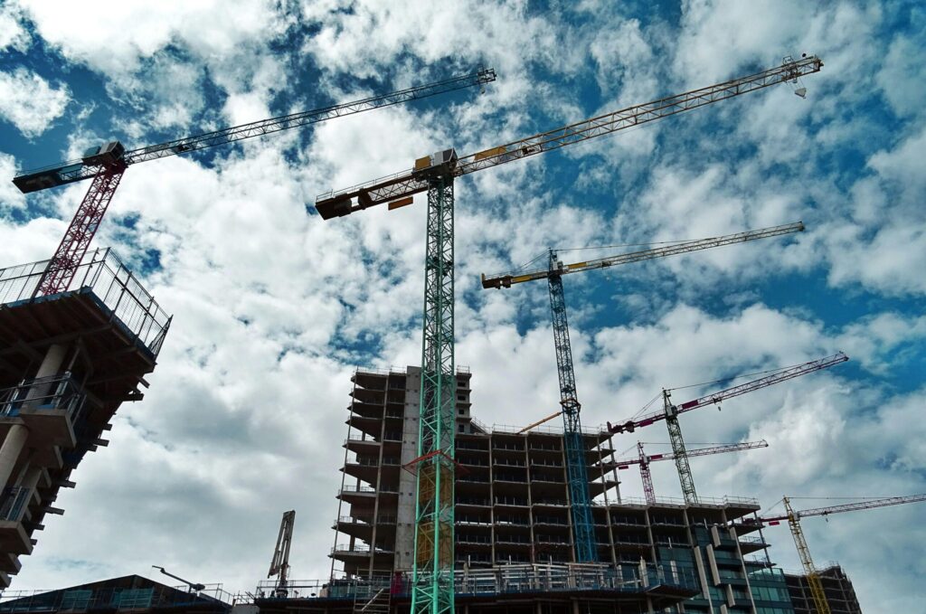 Urban construction site with numerous cranes framing rising skyscrapers against a blue sky.